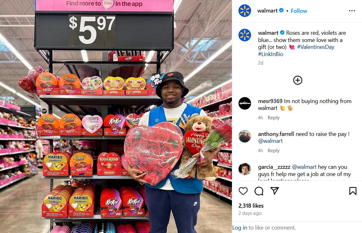 A Walmart employee holds a teddy bear, flowers, and a heart-shaped candy box in front of a Valentine