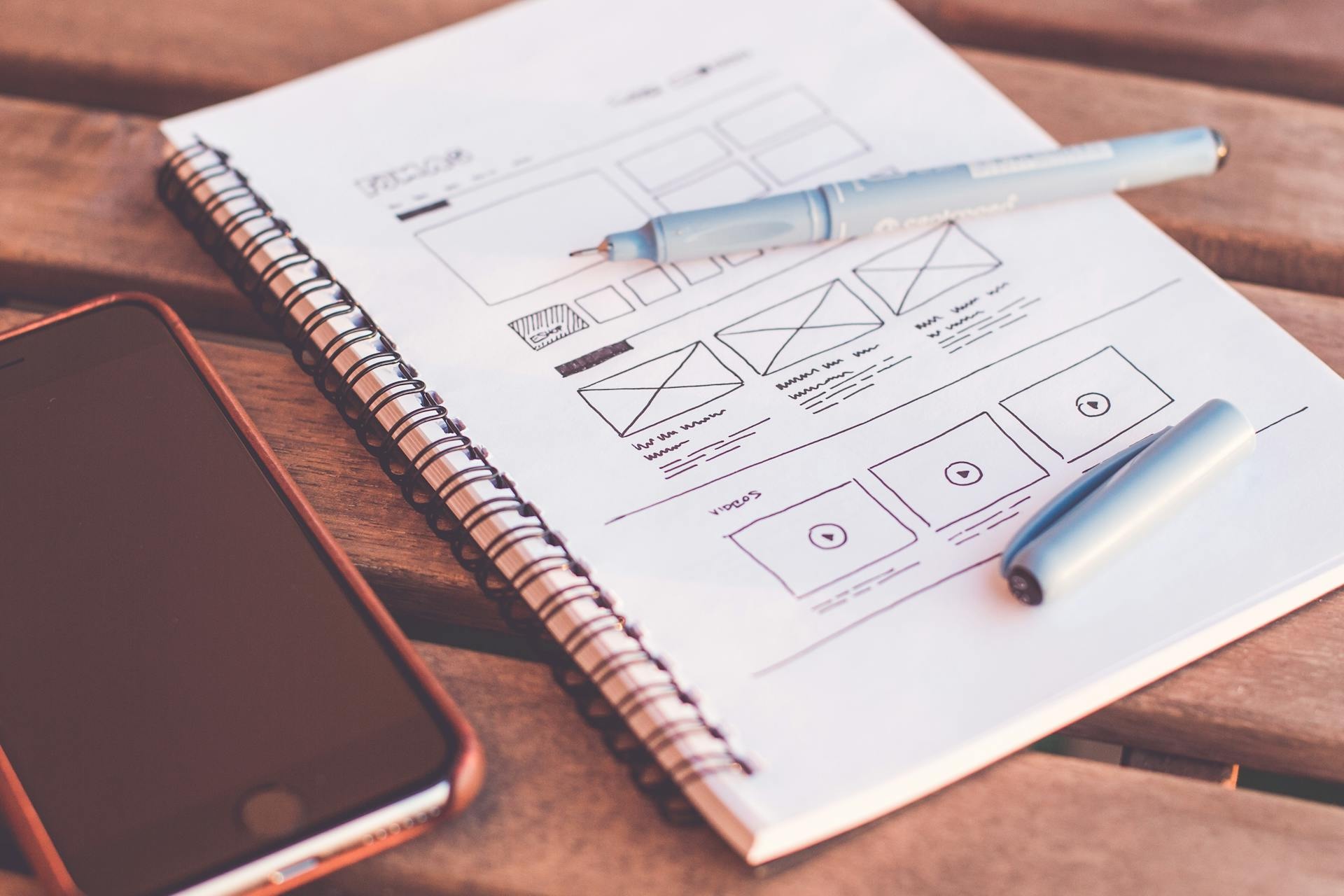 Hand-drawn website wireframe in notebook beside phone, planning sales page copy