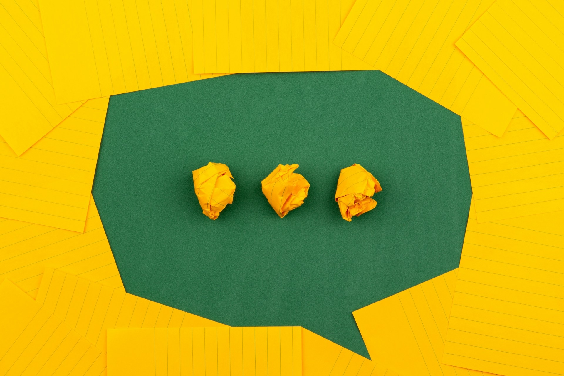 Orange sheets of paper lie on a green school board and form a chat bubble with three crumpled papers.